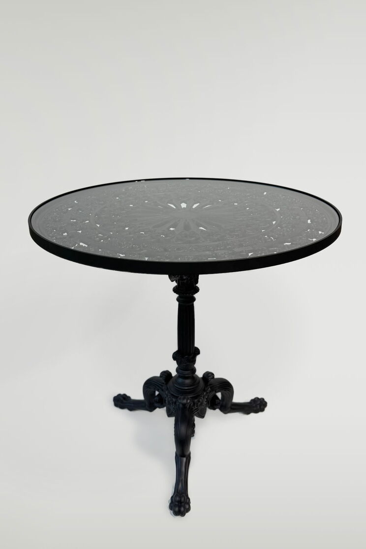 Round table with a glass top and an ornamental cast-iron base supported by three curved legs
